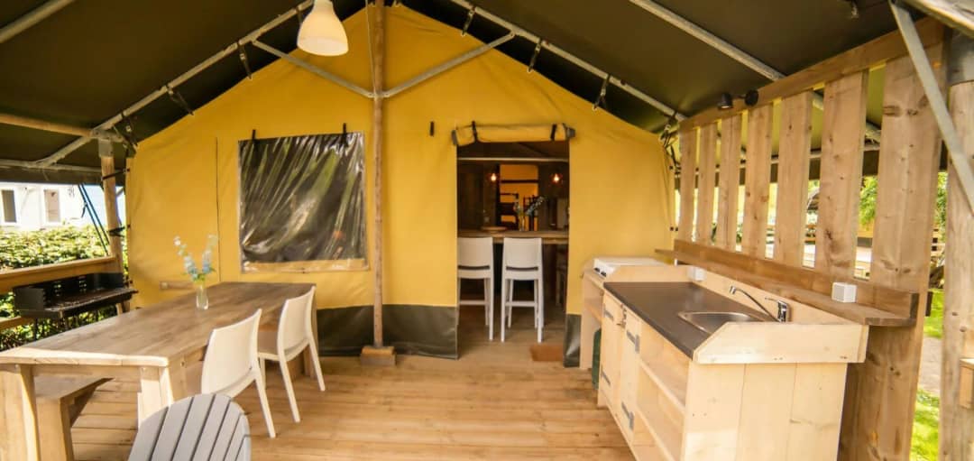 Überdachte Veranda der Safari Lodge mit einem Esstisch aus Holz, weißen Stühlen, einer Außenküche mit Spülbecken und einem Grill
