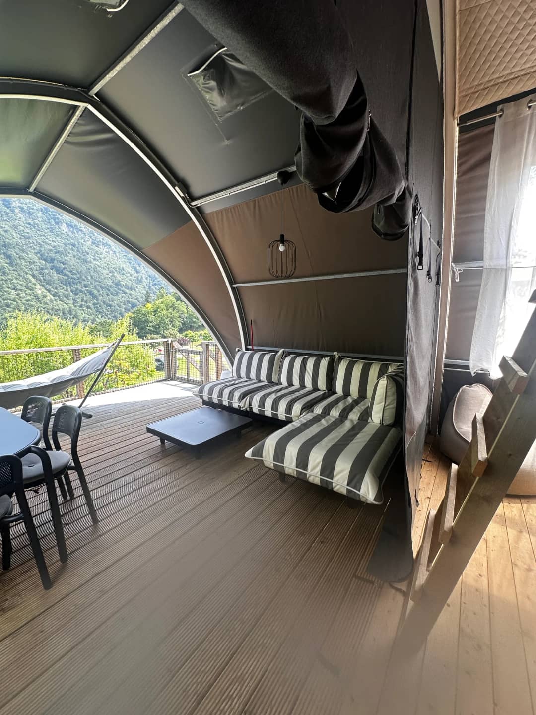 Überdachte Veranda der Big Oak Lodge XL mit gestreiftem Loungesofa, Couchtisch und Esstisch, mit Blick auf die Berge