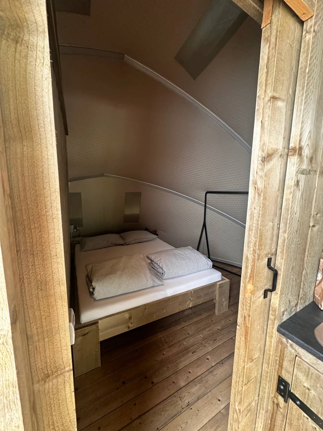 Schlafzimmer der Big Oak Lodge XL mit einem Doppelbett aus Holz unter der geschwungenen Wand, Blick durch den Türrahmen