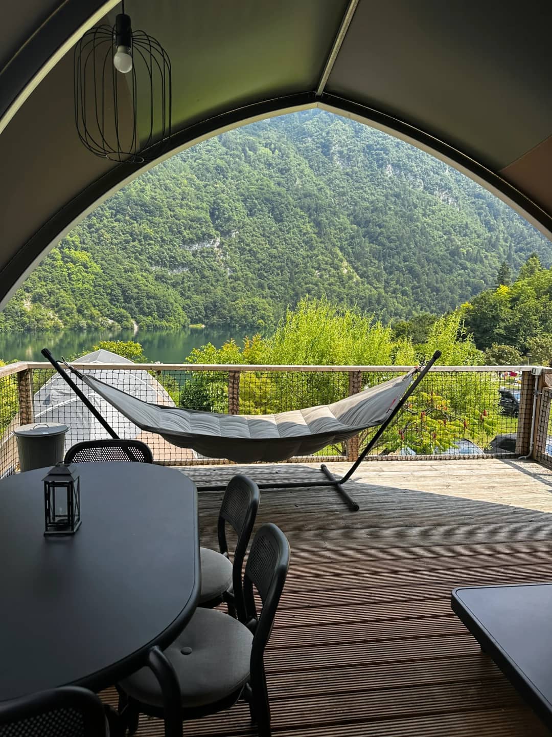 Hängematte und Esstisch mit Laterne auf der Veranda der Big Oak Lodge XL, mit Blick auf den See und die Berge