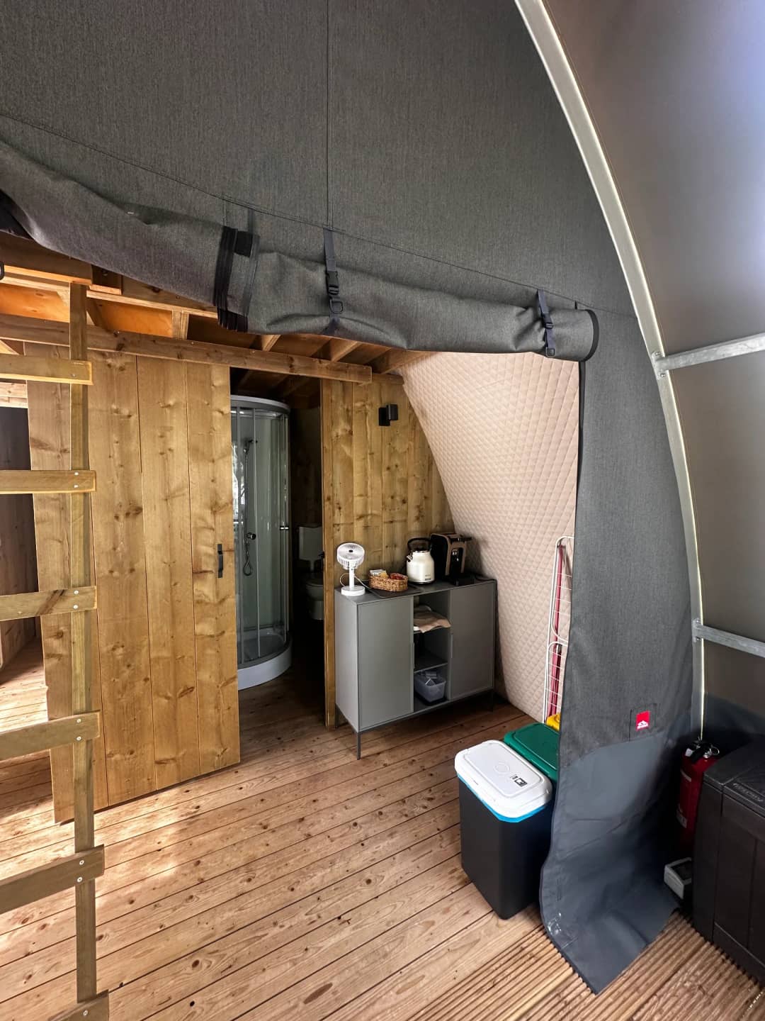 Im Inneren der Big Oak Lodge XL: eine Holztür zur Duschkabine und ein Schränkchen mit Wasserkocher und Toaster